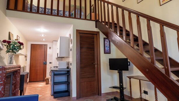 A staircase with wooden railings leading to an upper floor. A door with a window is visible on the left, and a television is mounted on the wall to the right.