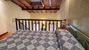A bedroom with a bed, wooden ceiling beams, a staircase, and a wall with a patterned wallpaper.