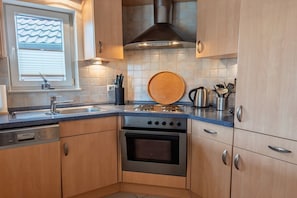 A modern kitchen with a dishwasher, stove, oven, and a window with blinds.