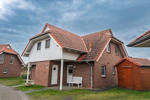 A two-story house with a red-tiled roof, a white exterior, and a small attached garage.