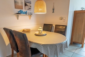 A dining area with a checkered tablecloth, a wicker pendant light, and a wall-mounted shelf with decorative items.