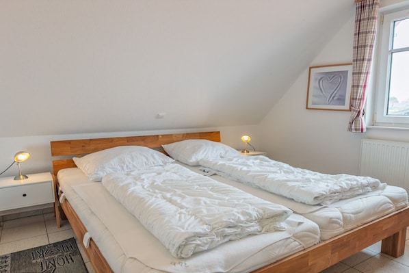 A bedroom with two single beds, a nightstand with a lamp, a radiator, and a window with a heart-shaped decoration.