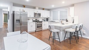 A modern kitchen with white cabinets, stainless steel appliances, and a central island with bar stools. - Comfy Unit Loft 15 min to EWR (Newark)