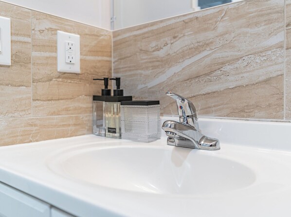 A bathroom with a white sink, a modern faucet, and beige marble tiles. - Comfy Unit Loft 15 min to EWR (Newark)
