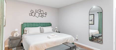 A bedroom with a bed, bedside tables, a bench, a mirror, and a geometric wall art piece.