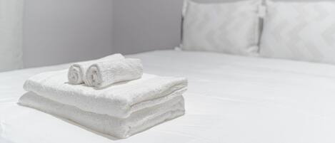 Una cama bien hecha con sábanas blancas y dos toallas enrolladas encima.