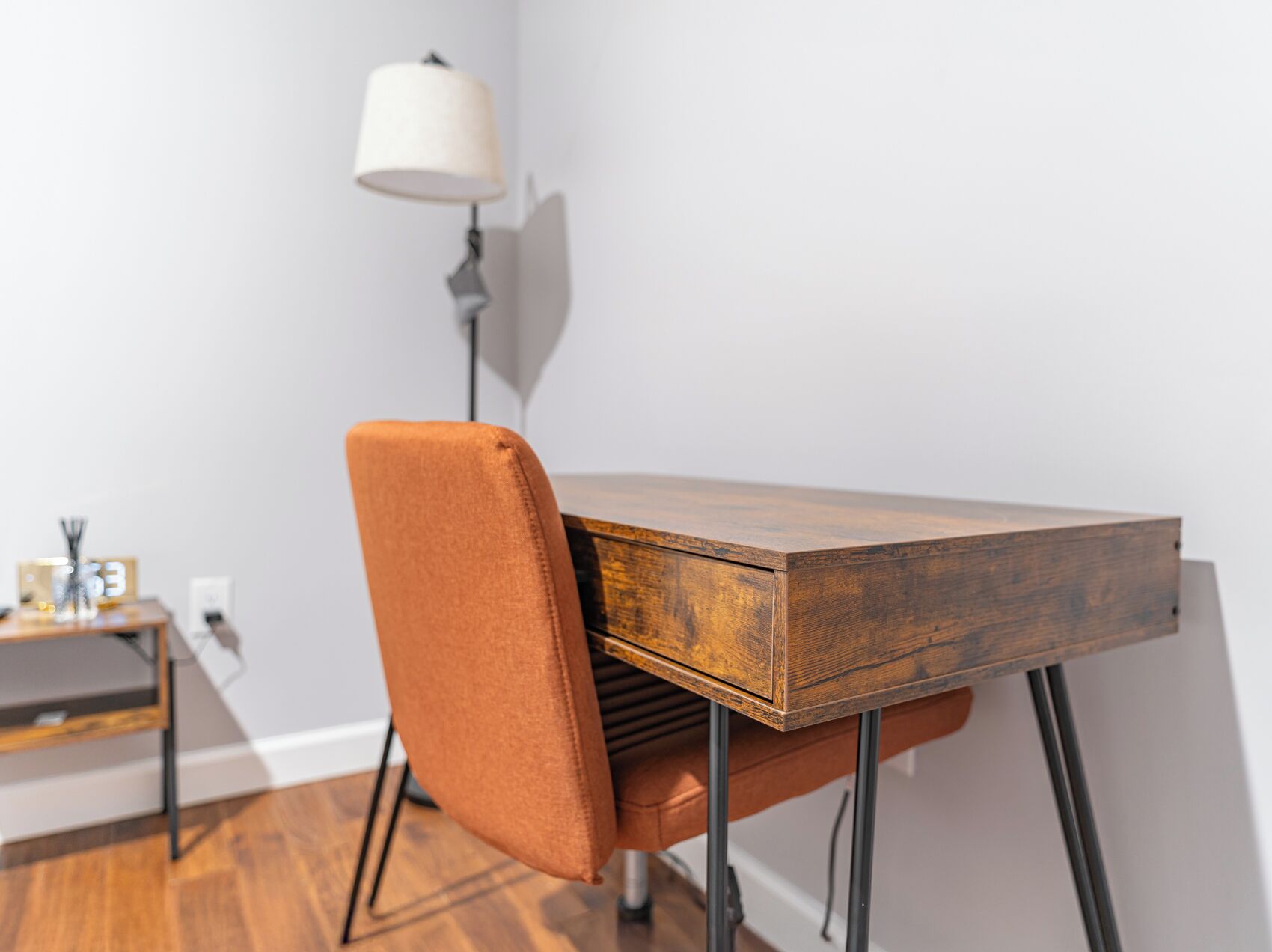 A wooden dining table with a single orange chair, a lamp, and a small table with a clock and decorative items.