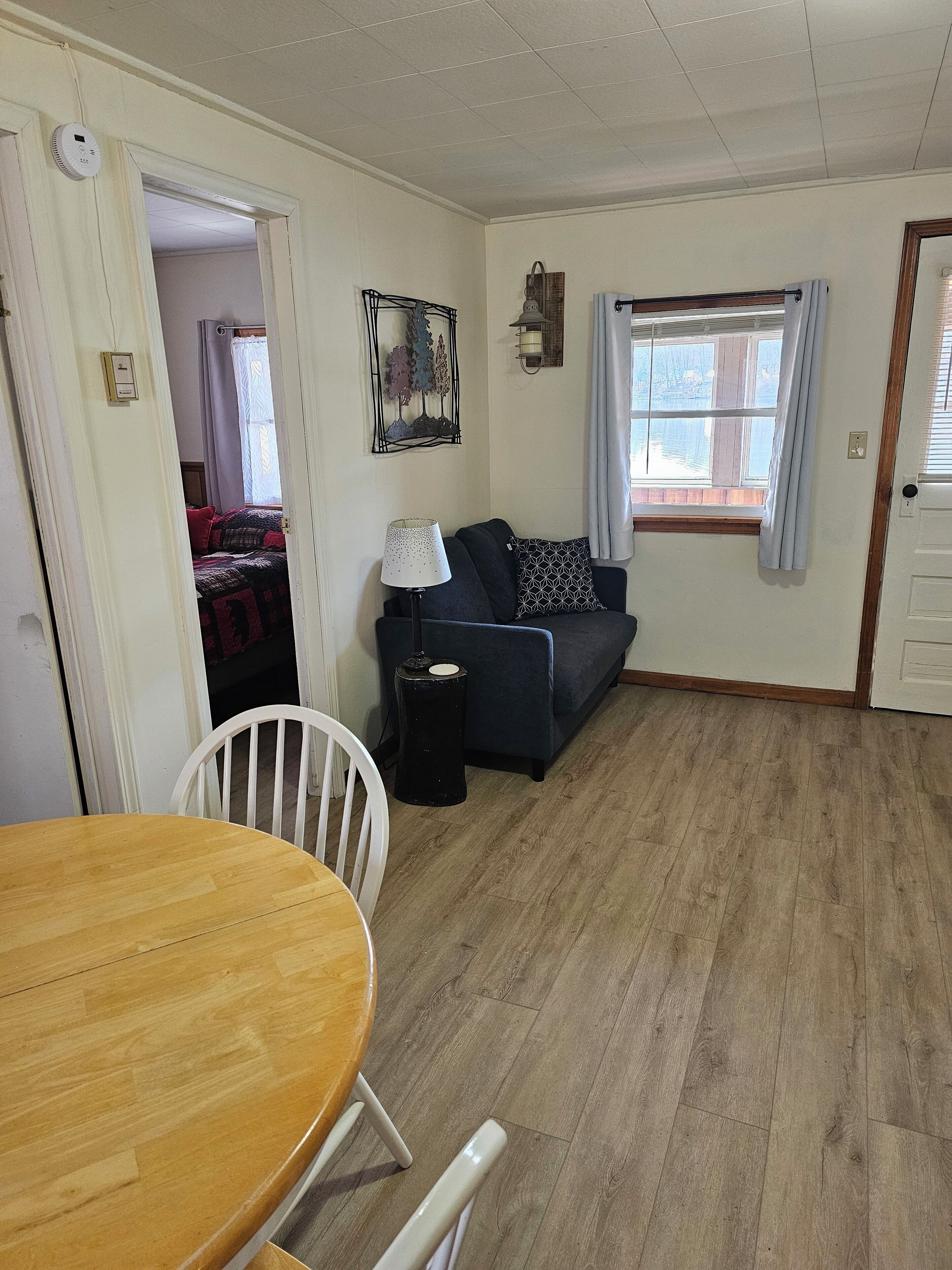 Una sala de estar con piso de madera, un sofá, una lámpara y una mesa de comedor con sillas.