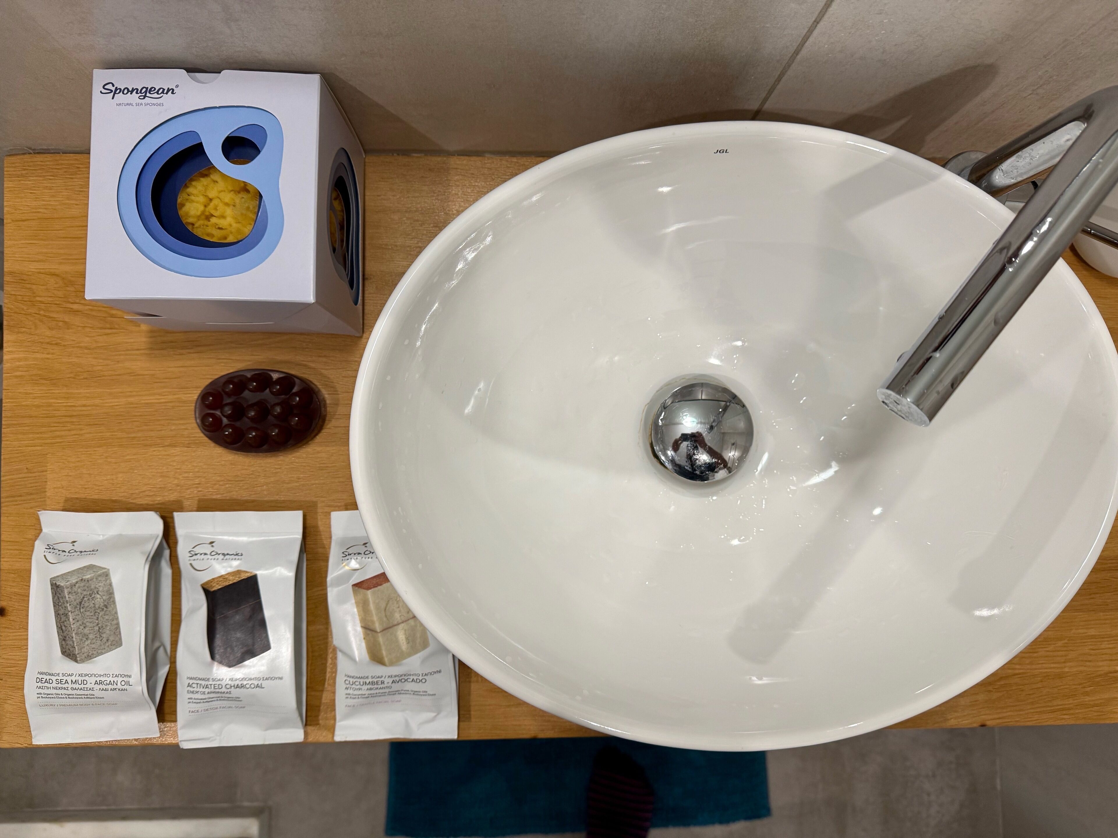 A bathroom sink with a box of Spongean soap, a bar of Dead Sea mud soap, a bar of activated charcoal soap, and a bar of Cucumber & Avocado soap.
