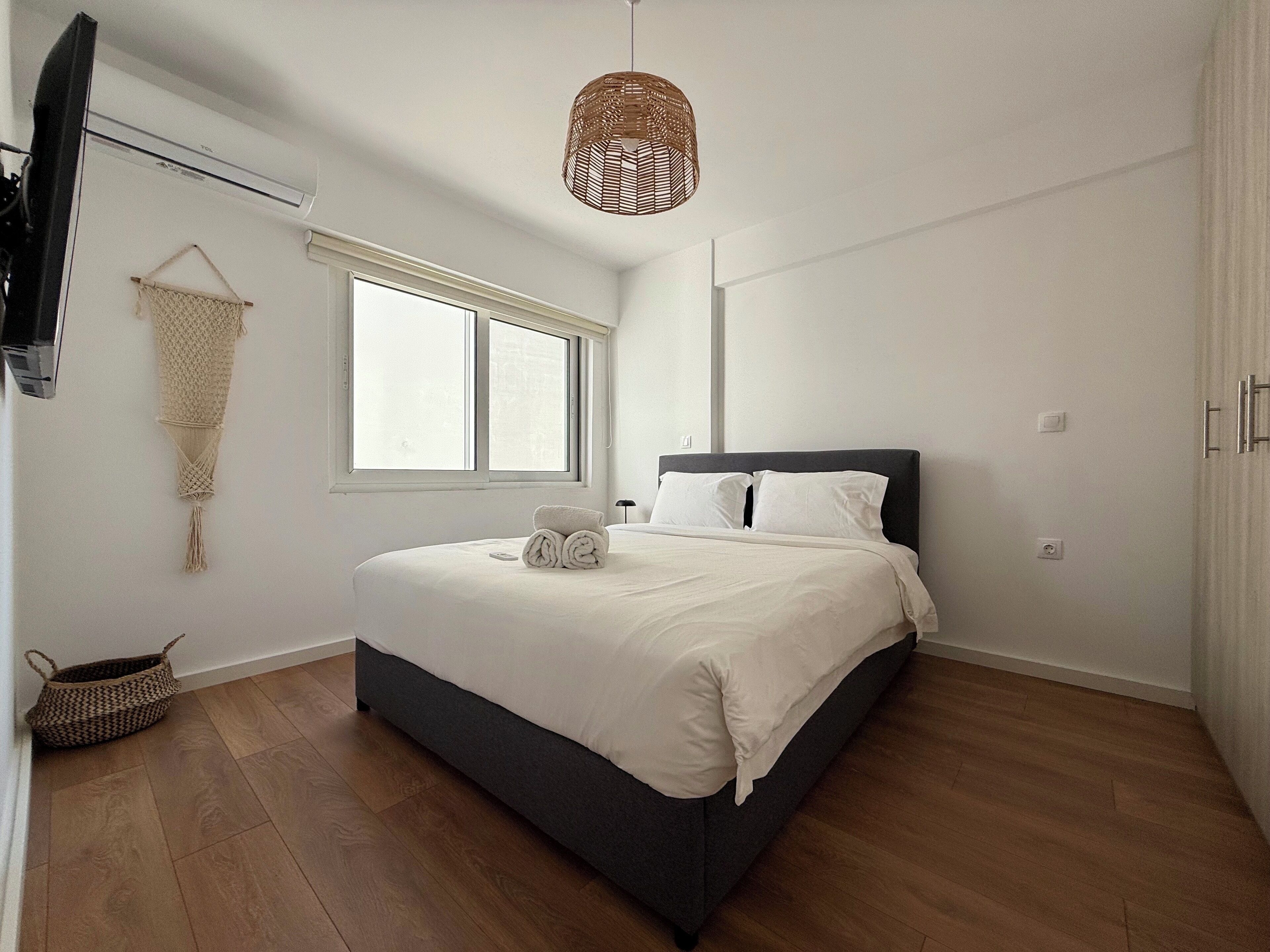 A bedroom with a bed, a hanging light fixture, a window, and a wall-mounted TV.