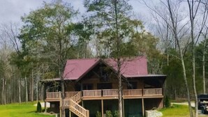 A cabin with a red roof, wooden deck, and a view of a lake.