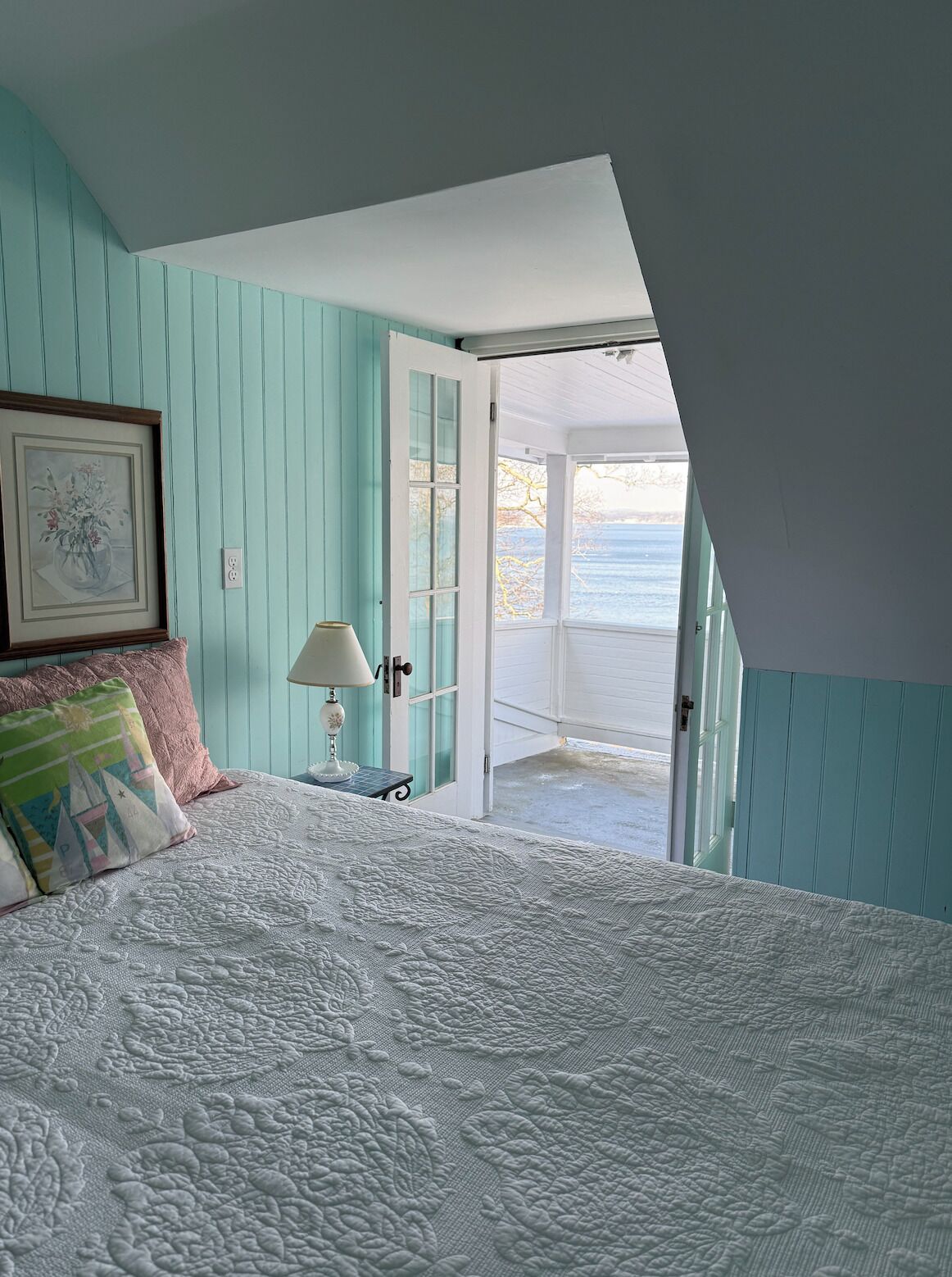 Une chambre à coucher comprenant un lit, une table de chevet, une lampe et une porte donnant sur un balcon.