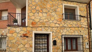 A two-story stone building with a balcony, a small window, and a door with a patterned curtain. - Rural house los jesuses (Lillo)