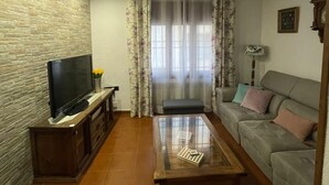 A living room with a flat-screen TV on a wooden cabinet, a glass coffee table, a sofa with cushions, and a stone-textured wall. - Rural house los jesuses (Lillo)