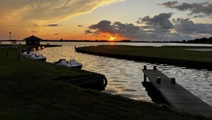 A sunset over a calm river with boats docked, a grassy area, and a wooden pier. - NEW! Vacation home Nordlicht (Südbrookmerland)