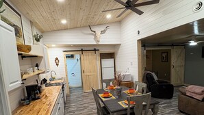A spacious kitchen with wooden flooring, a dining area with a table set for four, and a ceiling fan. - Sheltered Nook Bunk 'n Board
Farm to Table experience  (Molt)