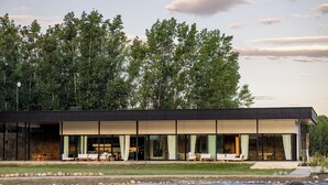 A modern building with a flat roof, large glass windows, and a patio area with outdoor seating. - House by Casa Septem (Tunuyan)
