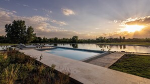 A swimming pool with lounge chairs and a view of a lake at sunset. - House by Casa Septem (Tunuyan)