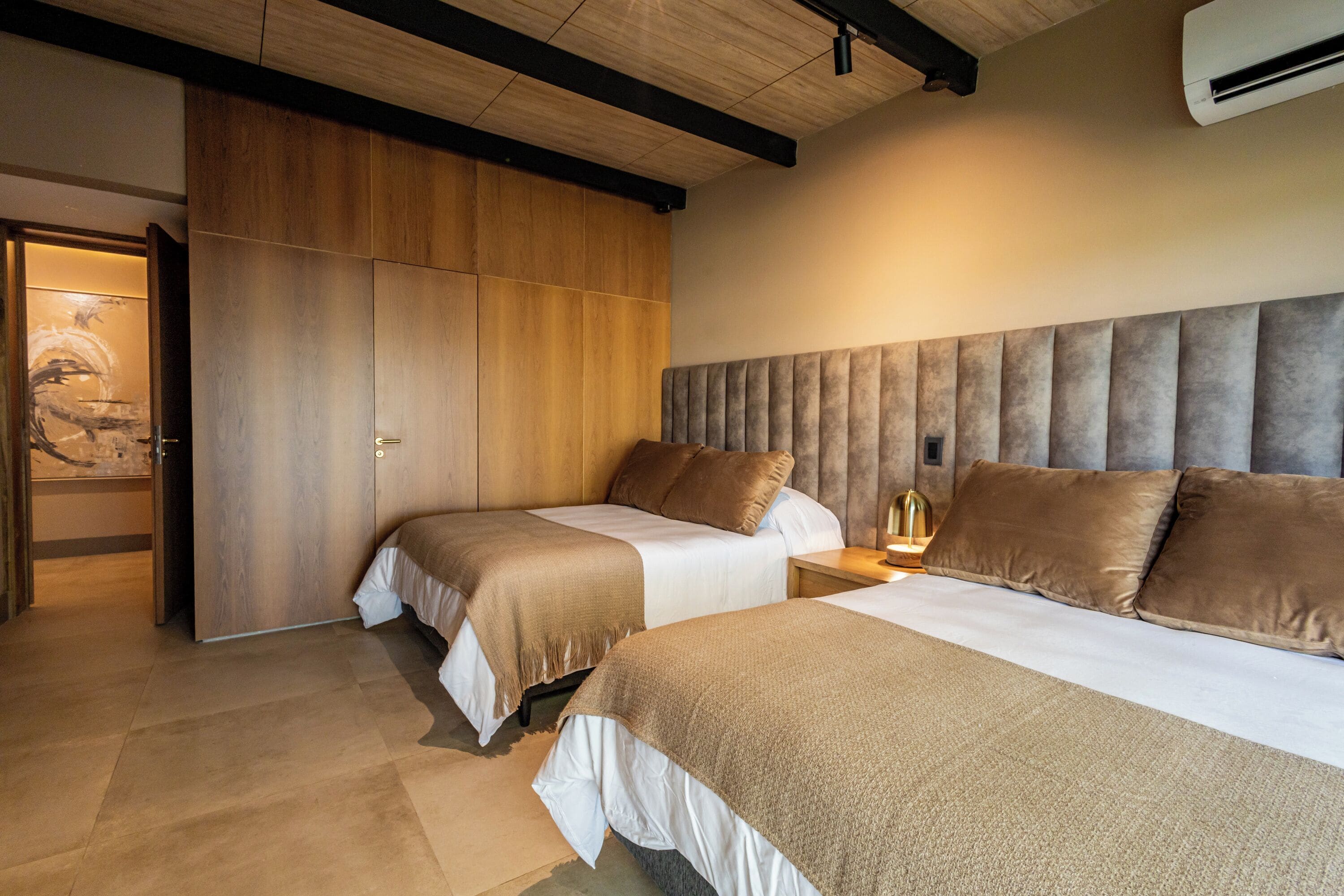 Une chambre avec deux lits, une armoire en bois et une tête de lit moderne.
