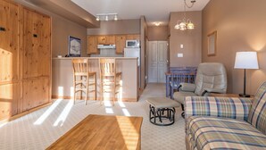 A cozy living room with a sofa, a wooden coffee table, and a kitchen area with wooden cabinets and a microwave.