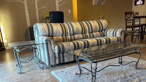 Ein Wohnzimmer mit einem gemusterten Sofa, einem Glastisch und einem Teppich.