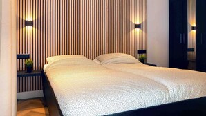 A modern bedroom with a bed, wooden slat wall, and two wall-mounted lights.