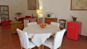 A dining area with a round table, white chairs, a red refrigerator, and a microwave on a wooden cabinet. - OPENSPACE APARTMENT WITH GARDEN KM 1.5 FROM THE SEA - OLEANDER (Rosignano Marittimo)