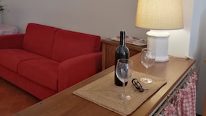 A small living area with a red sofa, a wooden table with a bottle of wine and glasses, a lamp, and a map on the wall. - OPENSPACE APARTMENT WITH GARDEN KM 1.5 FROM THE SEA - OLEANDER (Rosignano Marittimo)