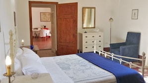 A bedroom with a bed, a dresser, a chair, a desk with a chair, and a dining area visible through an open door. - OPENSPACE APARTMENT WITH GARDEN KM 1.5 FROM THE SEA - OLEANDER (Rosignano Marittimo)