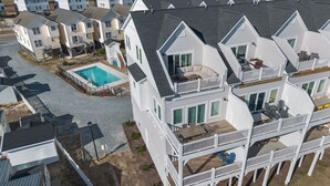 A multi-story residential building with a swimming pool, balconies, and a deck area. - Topsail Treasure: Elevator| Pool| Steps from Beach (Surf City)
