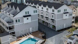 A residential complex with multiple houses, a swimming pool, and a view of the sea. - Topsail Treasure: Elevator| Pool| Steps from Beach (Surf City)