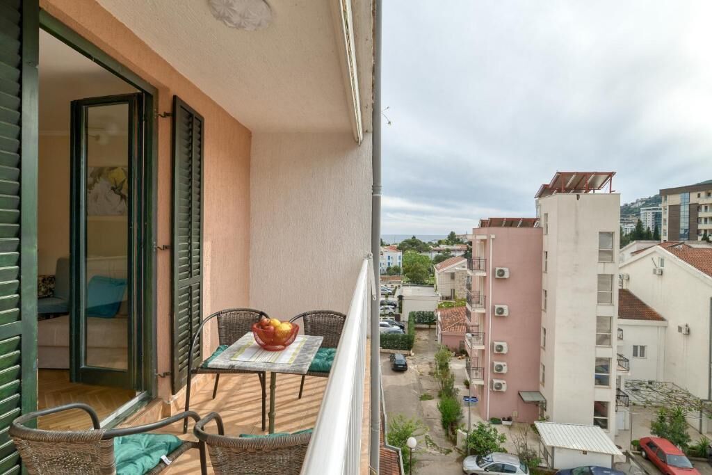 Een balkon met rieten meubels, een tafel met een schaal fruit en een uitzicht op de omliggende gebouwen.