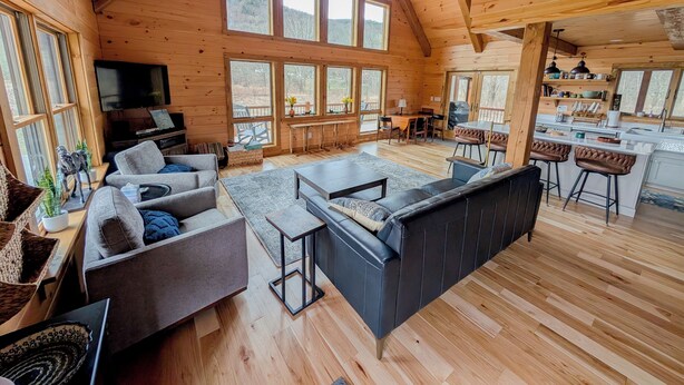 Een ruime cabin met een hoge nok, grote ramen, een gezellige zithoek met banken en een televisie, een eethoek met een tafel en stoelen, en een keuken met barstoelen.