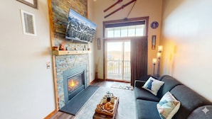 A cozy living room with a fireplace, a sofa, and a coffee table with pastries. - AS 434: Penthouse | Ballhooter Views | Cathedral Ceilings | Sleeps 6 (Snowshoe)