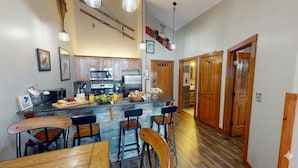 A modern kitchen with a central island, wooden bar stools, and a dining table. - AS 434: Penthouse | Ballhooter Views | Cathedral Ceilings | Sleeps 6 (Snowshoe)