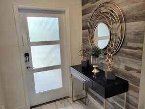 Enter through the stylish entryway featuring a frosted glass door and a console table with a mirror and decorative accents.
