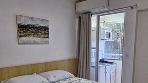 Une chambre à coucher avec un lit, un tableau, un appareil de climatisation et une vue sur l’extérieur.