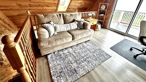 A cozy room with a wooden ceiling, a beige sofa, a small wooden table, and a large window with a view of a white fence.