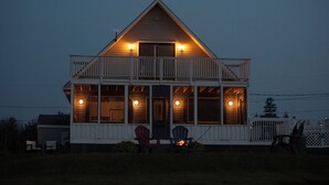 A two-story house with a balcony, a porch with chairs, and a fire pit.