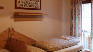 Una habitación con dos camas, techo de madera, un cartel del alfabeto enmarco y una ventana con cortinas.
