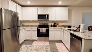 Cocina con armarios blancos, electrodomésticos de acero inoxidable, microondas, horno y lavavajillas.