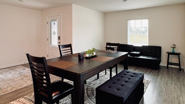 Un comedor con una mesa de madera, cuatro sillas, un banco y una mesita auxiliar con un florero.