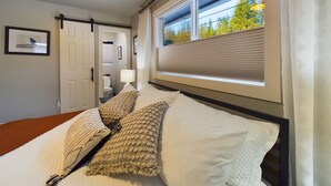 Ein Hotelzimmer mit Bett, Fenster mit Jalousien, einer Tür und einem gerahmten Bild an der Wand.
