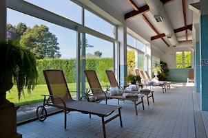 Een lichte binnenruimte met grote ramen, lounge fauteuils en uitzicht op een groen landschap.