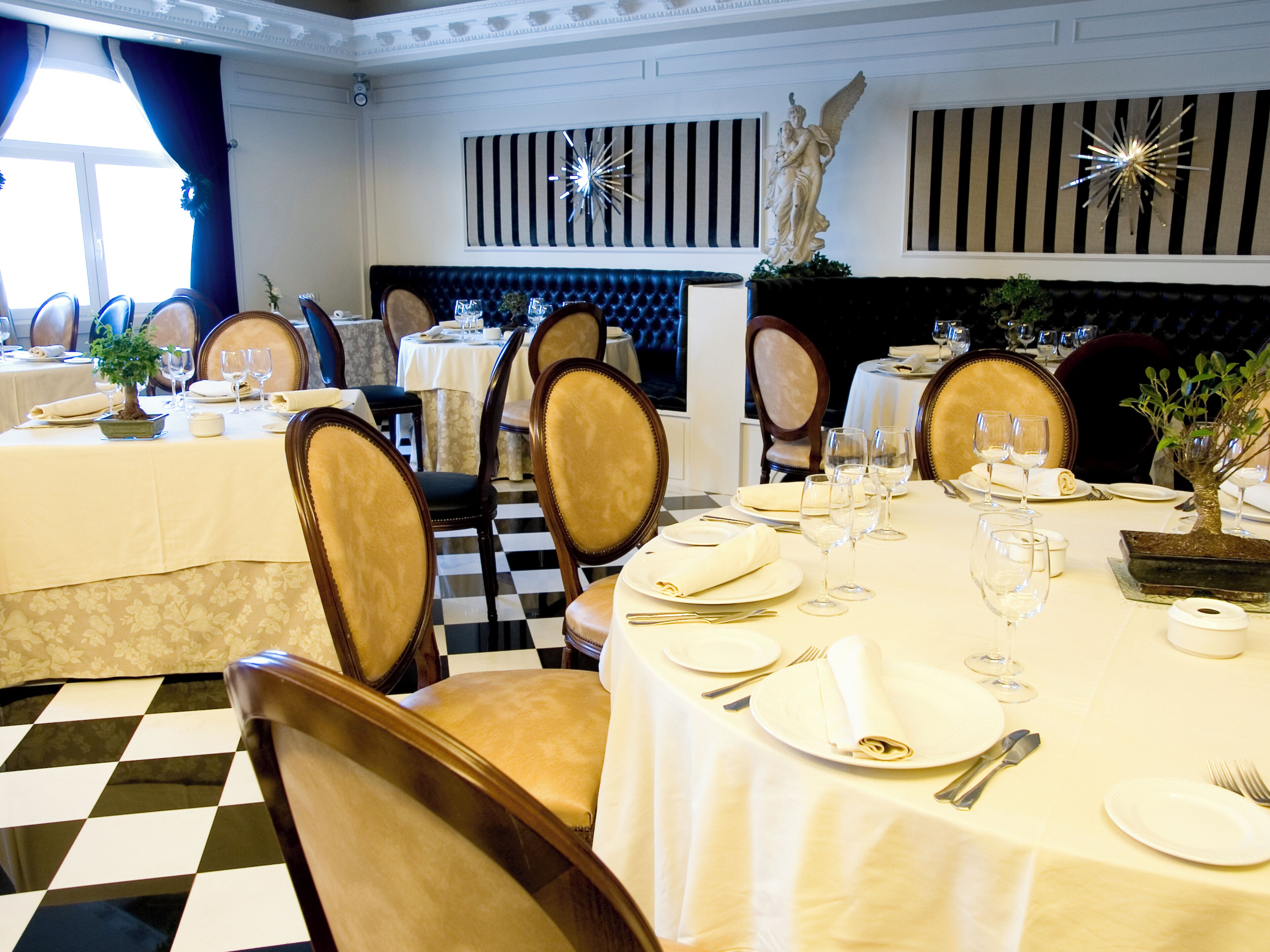 A formal dining area with checkered flooring, neatly set tables, and classic decor including a statue and striped wall panels.