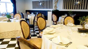 A formal dining area with checkered flooring, neatly set tables, and classic decor including a statue and striped wall panels.