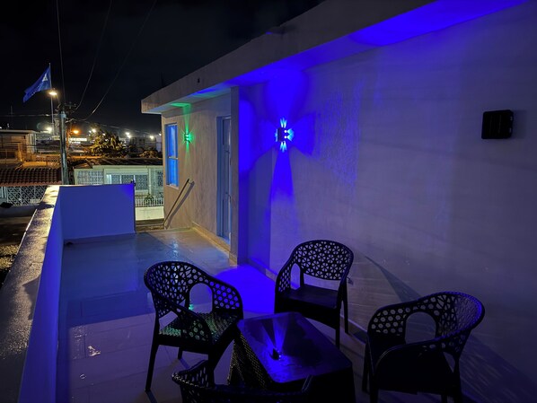 Un área de estar al aire libre con dos sillas y una mesa, iluminada con luces azules.