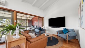 Uma sala de estar moderna com um sofá de couro, duas poltronas, uma mesa de centro e uma TV de tela plana fixada na parede.