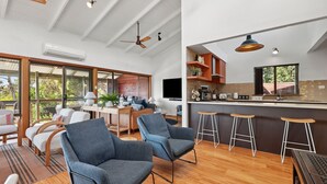 Uma sala de estar ampla com uma grande janela, uma cozinha com banquetas de bar e um ventilador de teto.