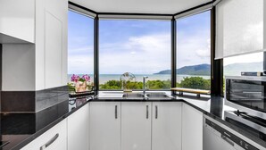 Eine moderne Küche mit einem großen Fenster und Blick auf das Meer und die Hügel.